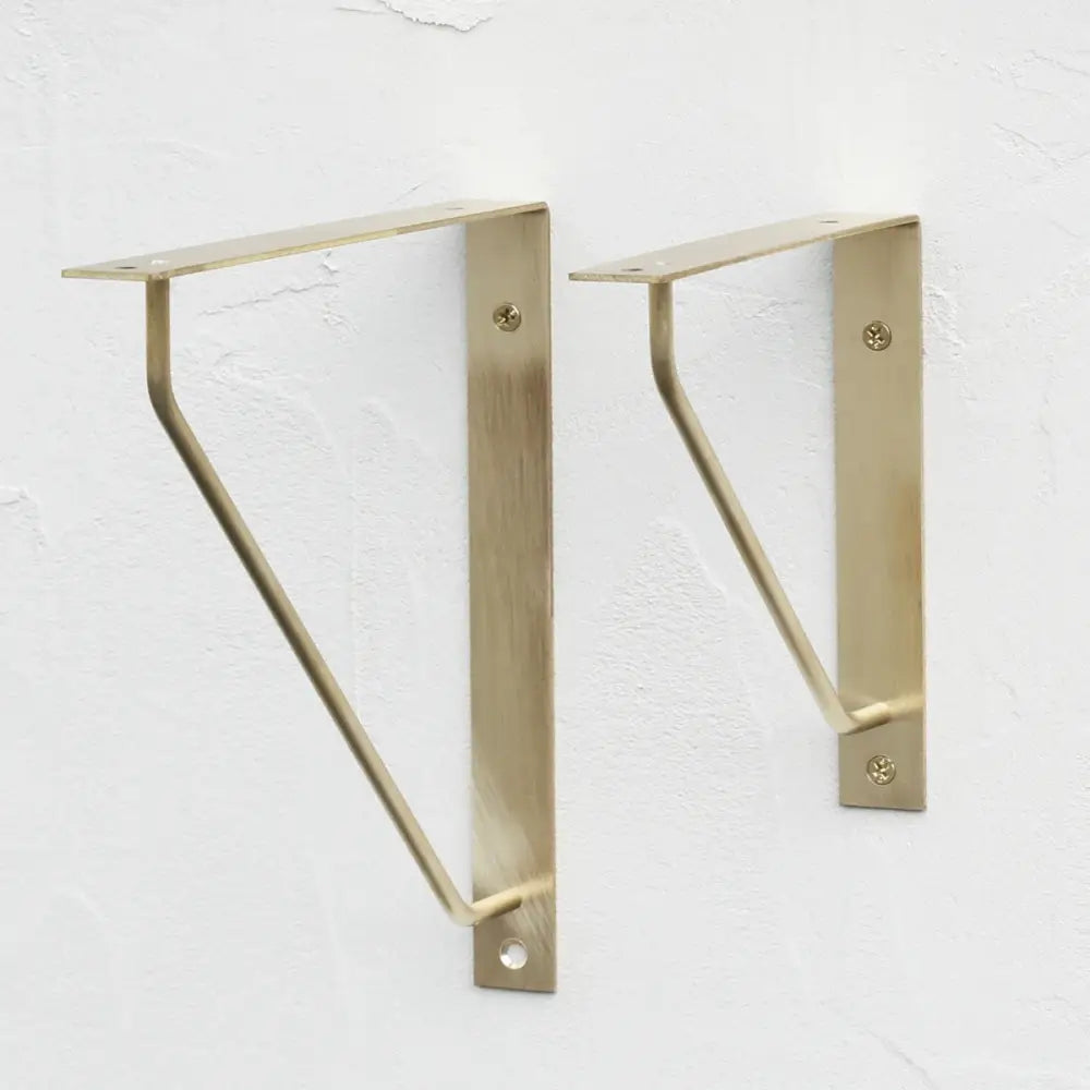 Antique brass triangle shelf bracket pair on wall, curved support arms visible