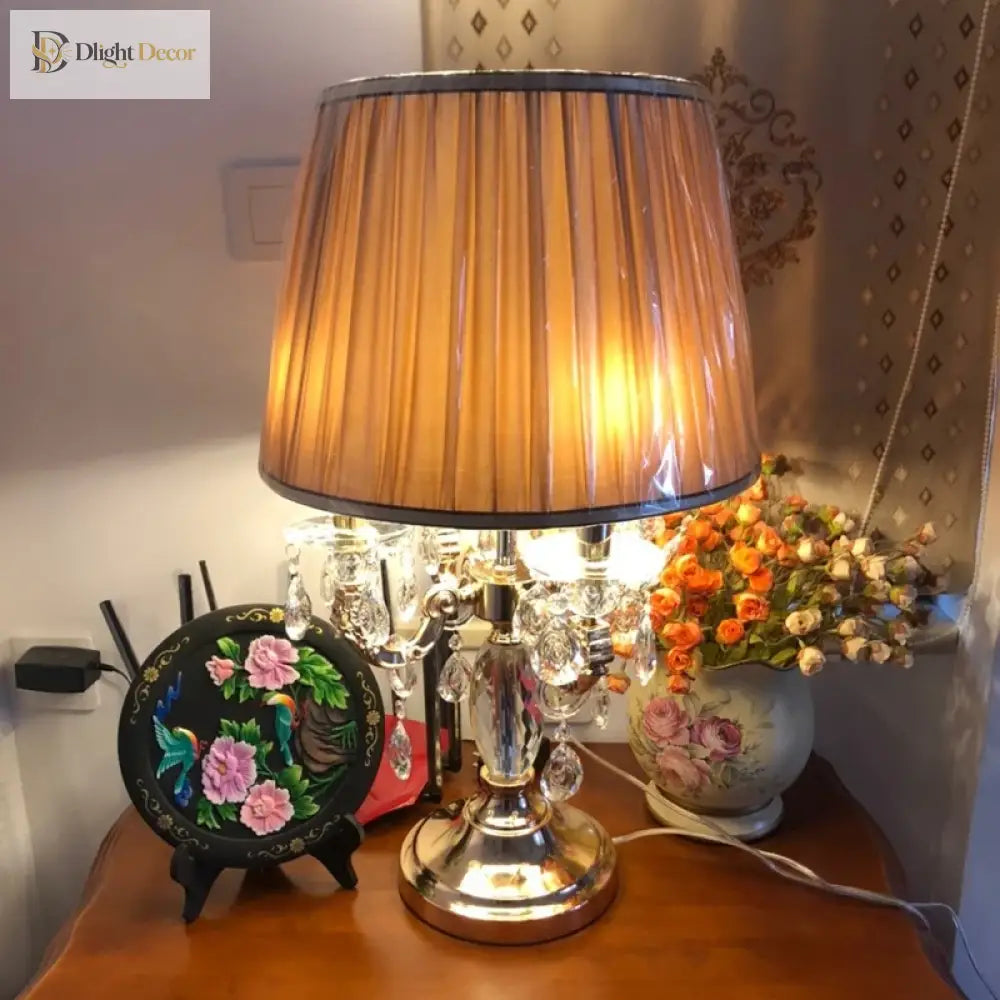 Gold crystal table lamp with amber pleated shade on bedside surface
