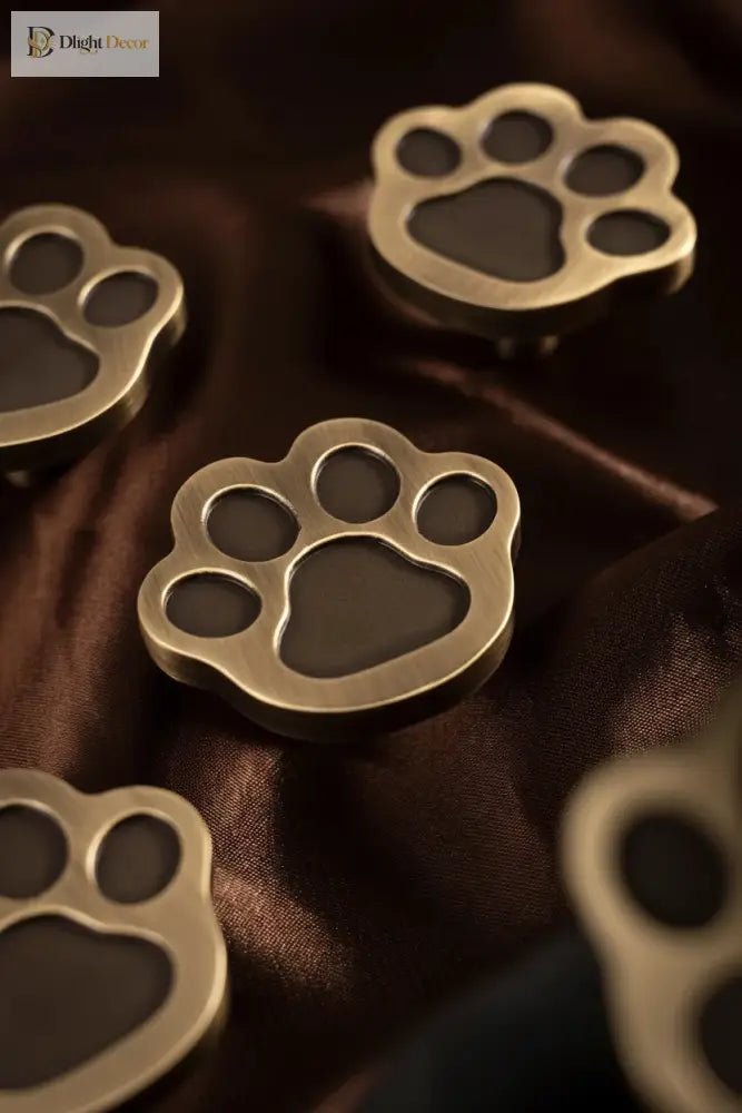 Brushed brass paw-print cabinet knobs with circular mounting post, decorative face details