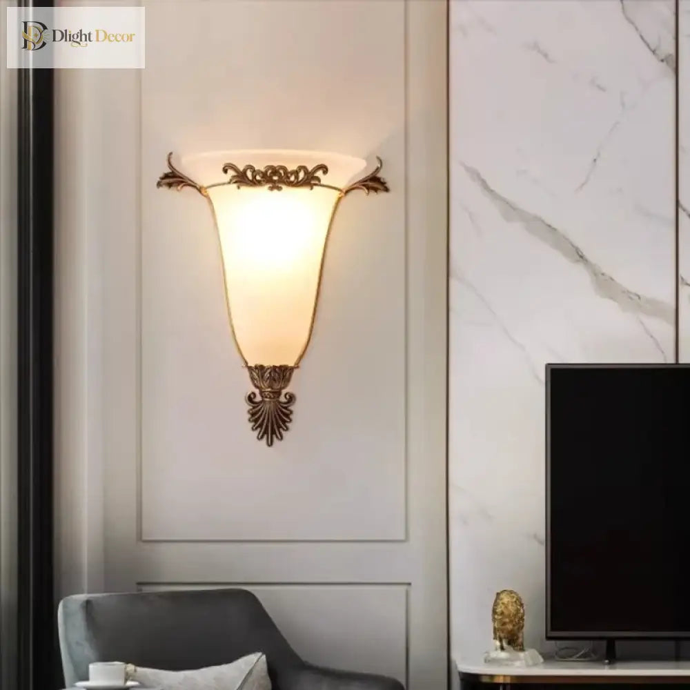 Decorative gold wall sconce with glowing frosted glass shade and carved metal crest