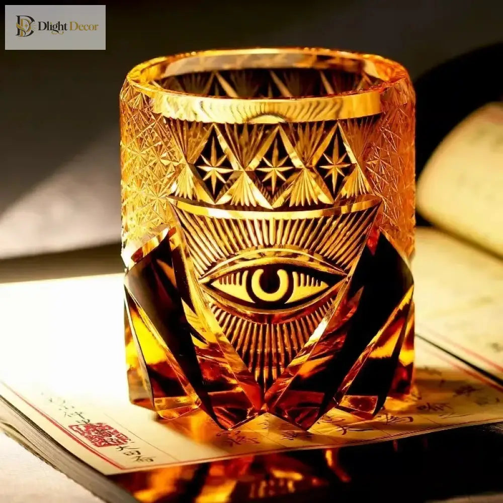 Amber-gold crystal whiskey tumbler with engraved eye emblem and diamond-cut texture