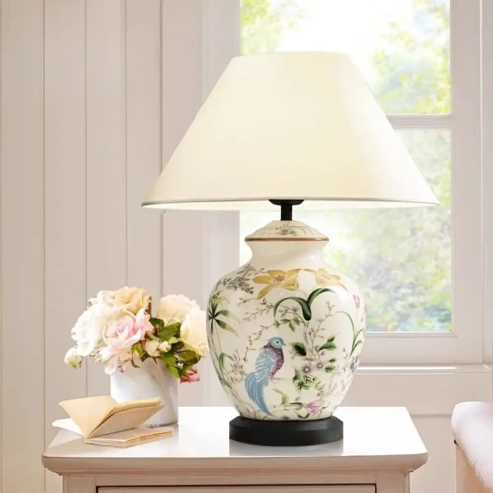 Flower-pattern ceramic table lamp with white shade and blue bird motif on a bedside table