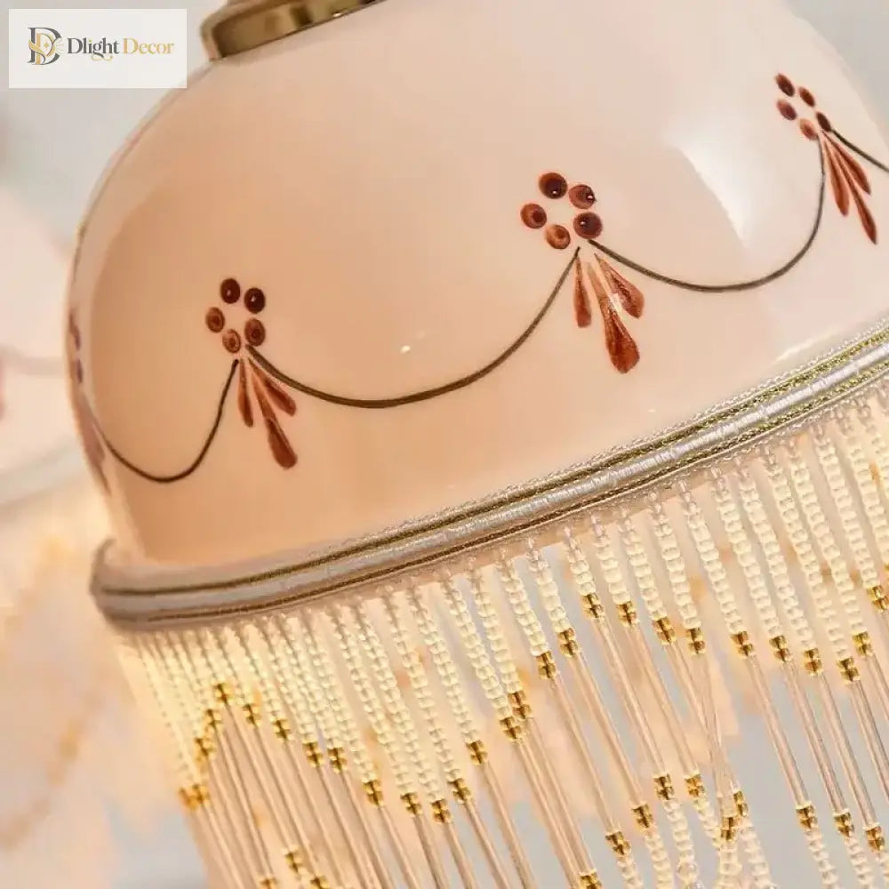 Close-up of white ceramic pendant shade with brown floral linework and golden fringe detailing