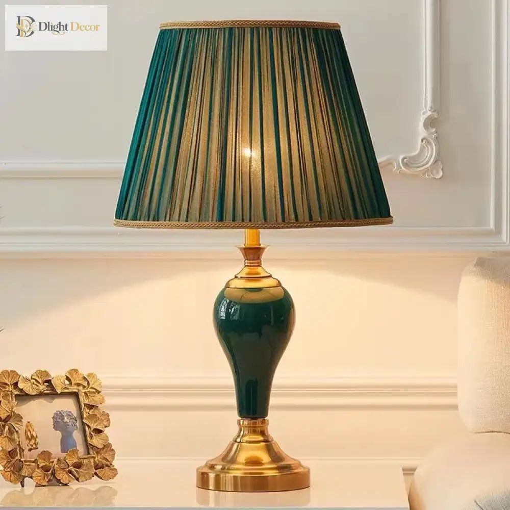 Green ceramic table lamp with pleated teal shade, gold base, and lit bulb glow
