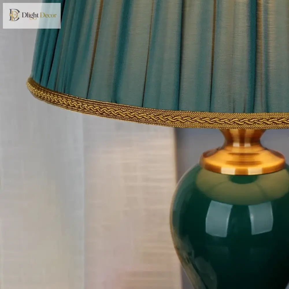 Pleated teal lamp shade with gold trim above a glossy green ceramic base