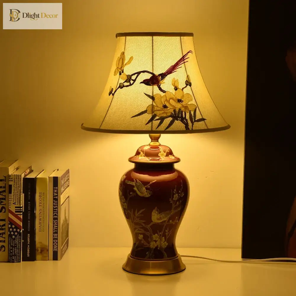 Ceramic LED desk lamp lit warmly, red vase with gold accents and cream floral shade