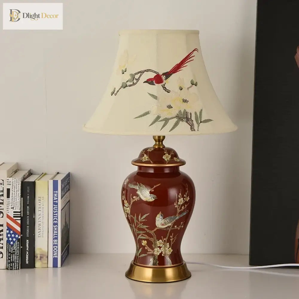 Ceramic LED desk lamp standing on a table with cream shade and red gold-patterned body
