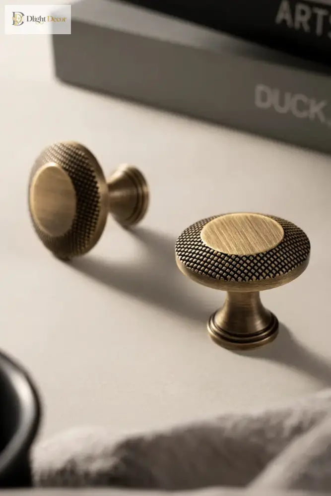 Antique brass cabinet knobs and a knurled grid bar pull on a drawer front.