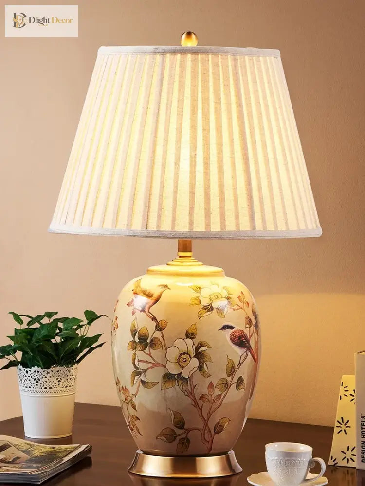 Ceramic table lamp featuring floral and birds artwork, pleated fabric shade, gold base