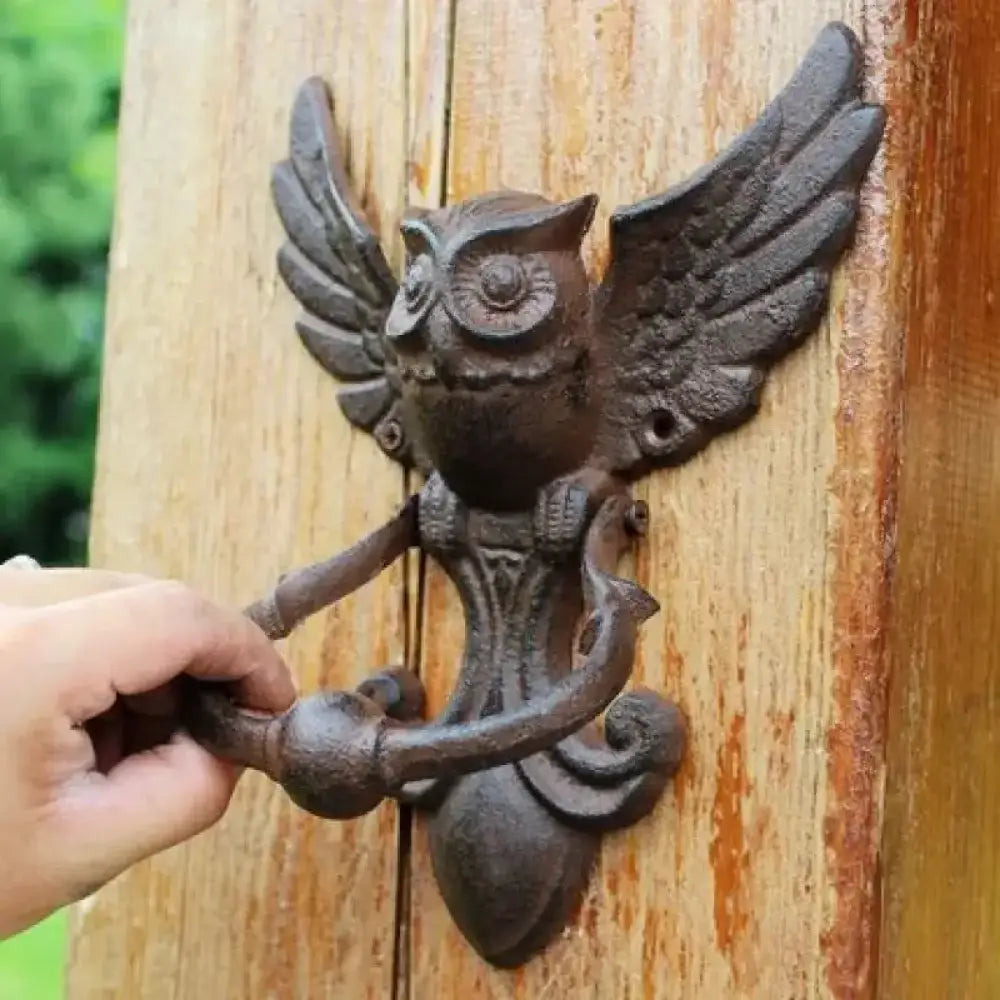 Cast iron owl door knocker with wings and curved handle, mounted on a wooden door