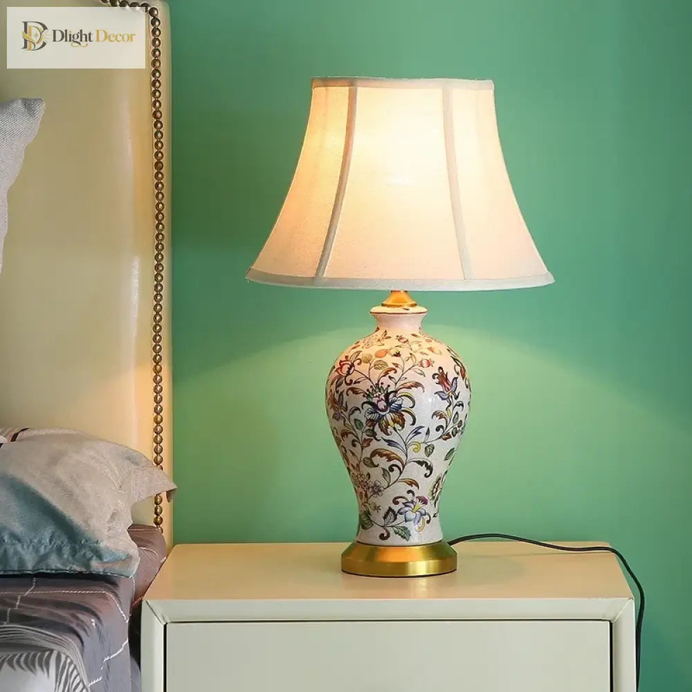 Floral ceramic table lamp with pleated white shade and brass base, power cord visible