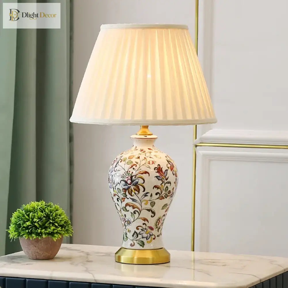 Floral ceramic table lamp with pleated white shade and gold base on tabletop.