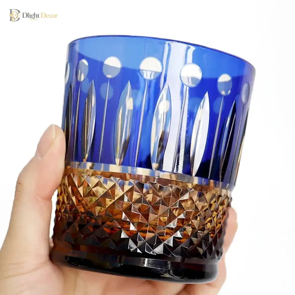 Blue diamond-cut crystal whiskey tumbler held in a hand, with gold-toned faceted band