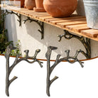 Close-up of iron tree-branch shelf brackets under a wooden ledge, dark bronze finish