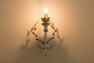 Gold and grey iron wall sconce with lit LED bulb and leaf wreath arms