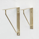 Antique brass triangle shelf bracket pair on wall, curved support arms visible