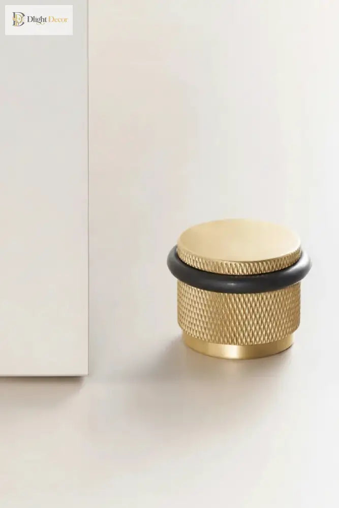 Adjustable knurled door stop with brass gold body and black top ring, floor-mounted