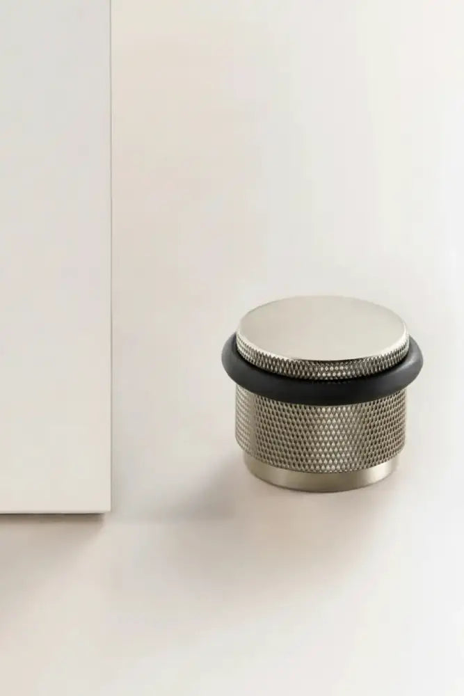 Adjustable knurled door stop with brushed metal body and black top ring, floor-mounted