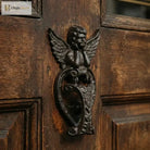Angel door knocker cast iron mounted on wood door with winged figure and heart base, dark