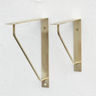 Antique brass triangle shelf bracket pair on wall, curved support arms visible