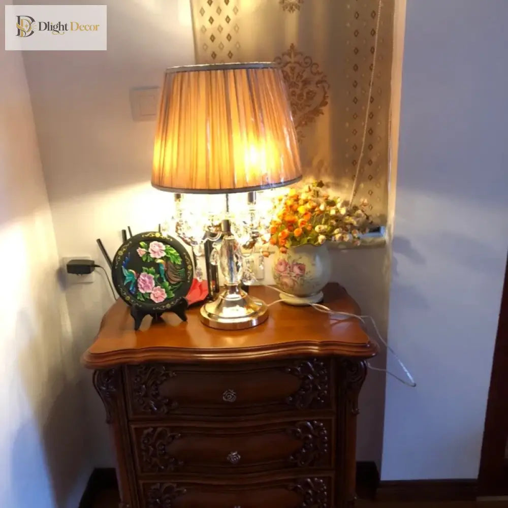 Gold crystal table lamp with amber drum shade on wooden nightstand