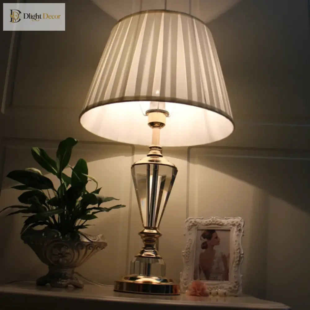 Crystal LED desk lamp with tall crystal stem and pleated white shade on tabletop