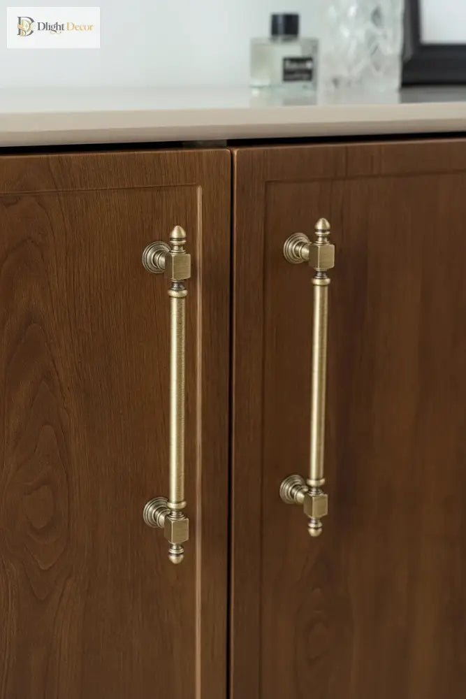Antique brass cabinet handles on two wooden cabinet doors with finial pulls