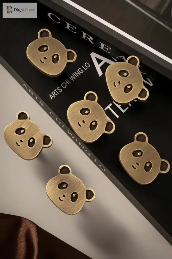 Set of brushed brass panda cabinet knobs with hanging bear-face and paw-print designs