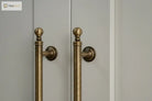 Brushed brass T-bar cabinet pull with round backplate and finial ends, wall mount