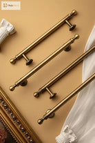 Pair of brushed brass T-bar cabinet pulls with knob-like finials and short pedestal bases
