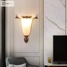 Decorative gold wall sconce with glowing frosted glass shade and carved metal crest