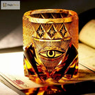Amber-gold crystal whiskey tumbler with engraved eye emblem and diamond-cut texture