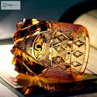 Amber-gold crystal tumbler showing engraved eye design and geometric facets along the side
