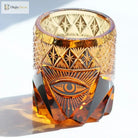 Amber-gold crystal tumbler with engraved eye pattern and reflective faceted sides