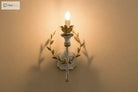 Gold and grey iron wall sconce with lit LED bulb and leaf wreath arms
