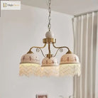 Gold three-head pendant light with white ceramic shades, brown floral trim, fringe tassels on chain