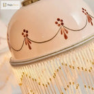 Close-up of white ceramic pendant shade with brown floral linework and golden fringe detailing
