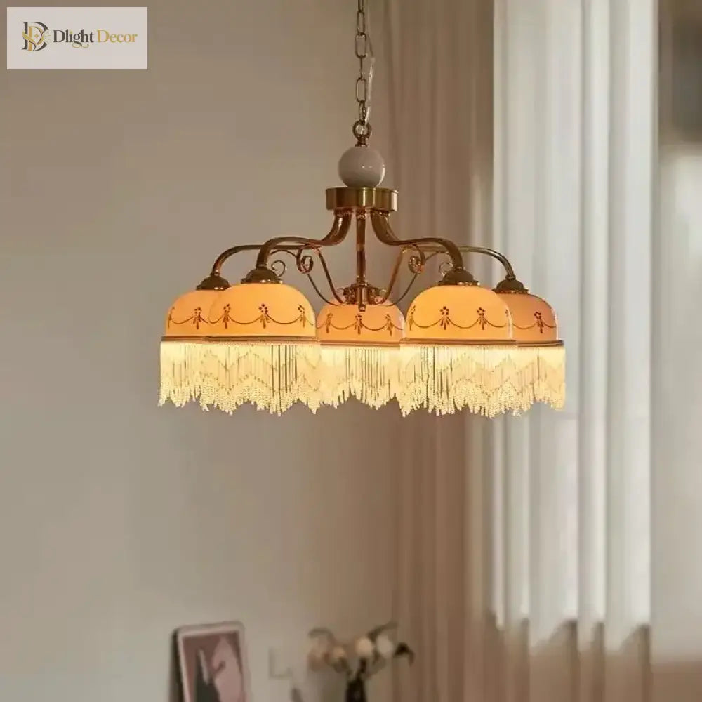 Gold three-head pendant light with white ceramic shades, brown floral trim, tassel fringe on chain