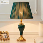 Green ceramic table lamp with pleated teal shade, gold base, and lit bulb glow