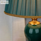 Pleated teal lamp shade with gold trim above a glossy green ceramic base