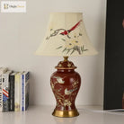 Ceramic LED desk lamp standing on a table with cream shade and red gold-patterned body