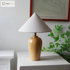 Wooden table lamp with white cone shade and brass stem on white shelf