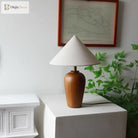 Wooden bedside lamp with white cone shade and brass neck beside green plant