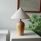Wooden table lamp with white cone shade and brass stem on white ledge