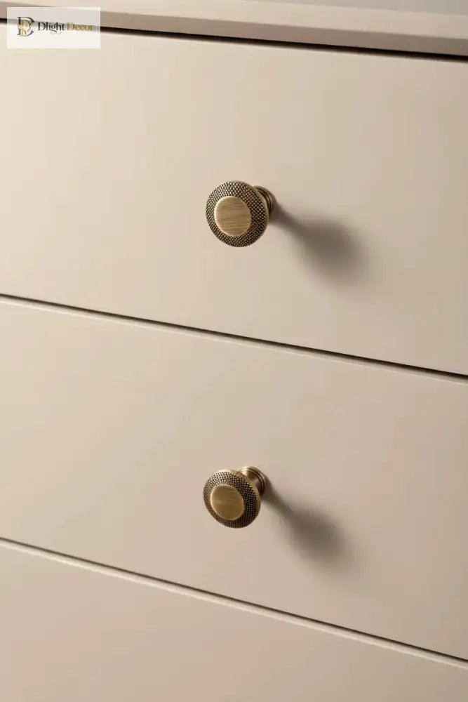 Two round cabinet knobs with knurled grid tops in antique brass on drawers.