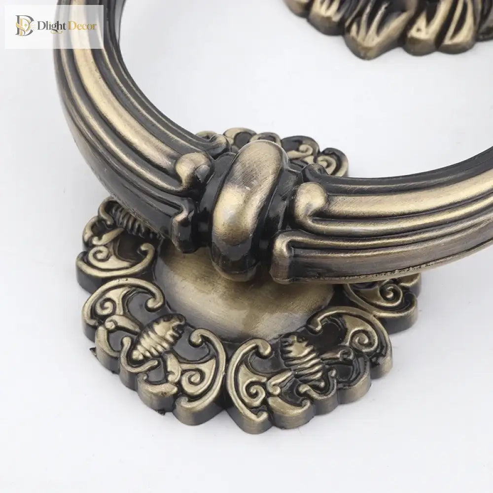 Close-up lion head door knocker ring with ornate scroll details, antique bronze