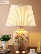 Ceramic table lamp featuring floral and birds artwork, pleated fabric shade, gold base