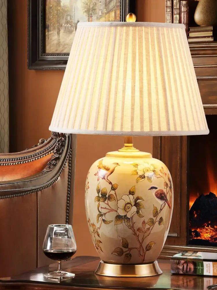 Ceramic table lamp with floral bird design, pleated fabric shade, gold base and finial
