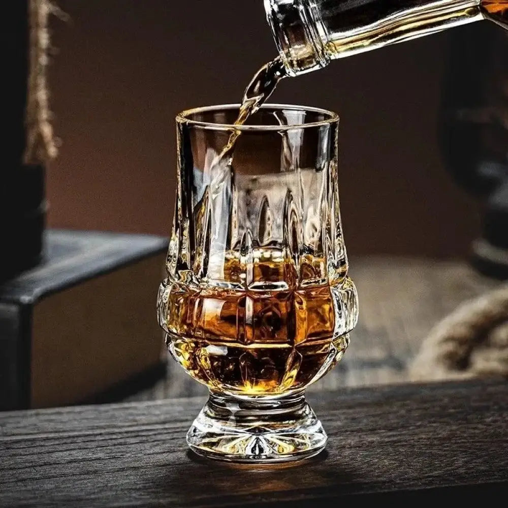Faceted crystal whiskey tasting glass with scrolled cut base, holds amber drink