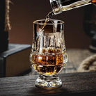 Faceted crystal whiskey tasting glass with scrolled cut base, holds amber drink